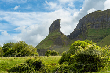 Obraz premium Eagle Rock towers above green fields and trees in County Sligo, Ireland, under bright broken clouds. A striking geological landmark in the Gleniff area.