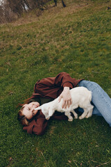 Obraz premium Young person lying on grass with playful goat kid, enjoying a relaxed outdoor moment, casual clothing, gentle interaction and affection in a tranquil park