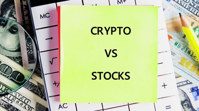 A yellow sticky note with Crypto vs Stocks emerges on a desk resting on US Dollar bills and a calculator A magnifying glass is also seen
