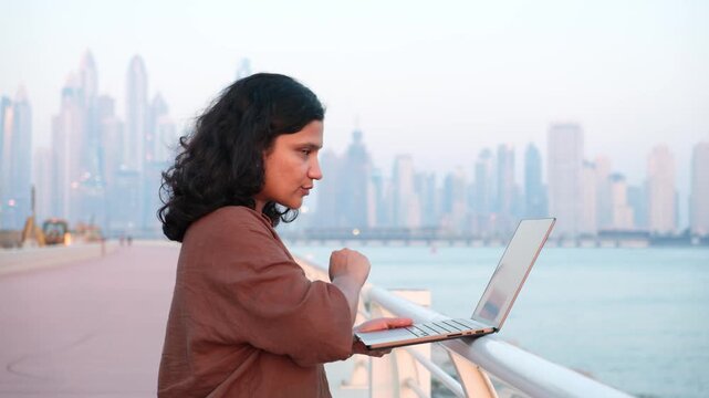 Modern professional attending virtual meeting remotely during waterfront staycation with Dubai skyline footage