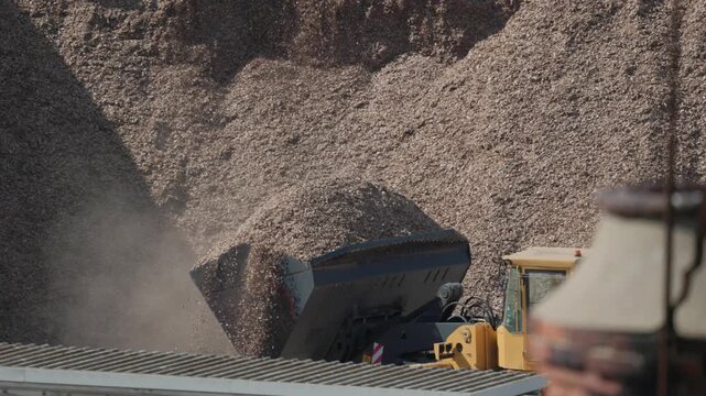Heavy machinery moves large piles of wood chips at a processing site in the afternoon sun