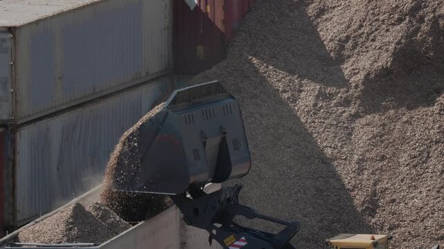 Heavy machinery loads wood chips at a processing facility in a busy industrial area
