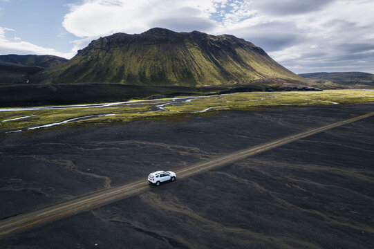 Aerial view of a white SUV driving on the F235 road through a vast volcanic landscape with black sand and mossy mountains Highlands of Iceland, Iceland.