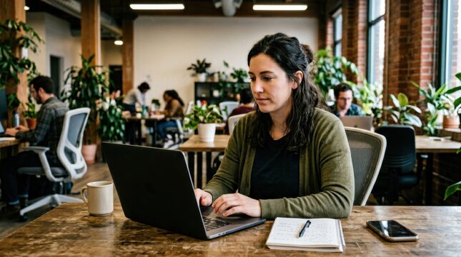 Authentic candid shot of a localization specialist editing confidential merger documents with a laptop privacy filter in a contemporary plantfilled coworking space featuring