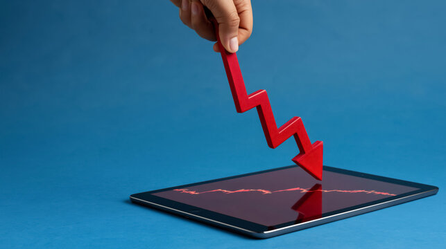 Hand holding red arrow over tablet displaying financial decline graph on blue background