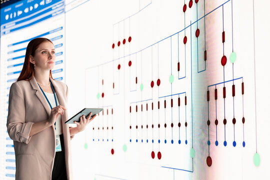 Reviewing PCB layout, tablet and female engineer looking at large digital screen. Electronic device manufacturing, electrical circuit connections and woman checking component placement