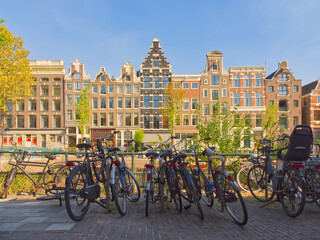 Fototapeta premium Traditional Dutch canal houses and bicycles parked along Amsterdam waterway on sunny day