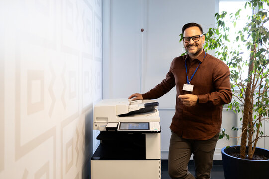 Happy male employee using modern multifunction printer in corporate office, smiling during work tasks.