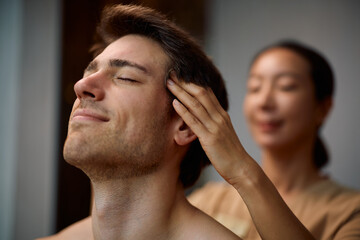 Fototapeta premium Smiling man receiving head massage at wellness spa.