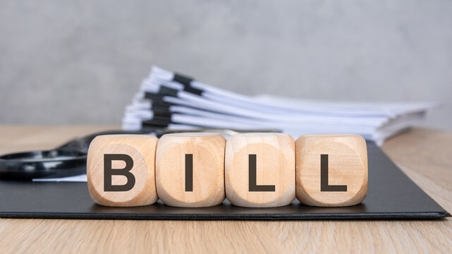 Wooden blocks with BILL text, blurred documents and magnifying glass.