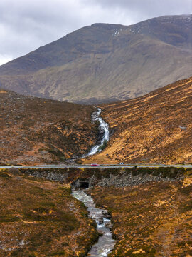 Aerial view of Eas a' Bhradain waterfall cascading down a rugged hillside towards a road with a red car Isle of Skye, Scotland, United Kingdom.