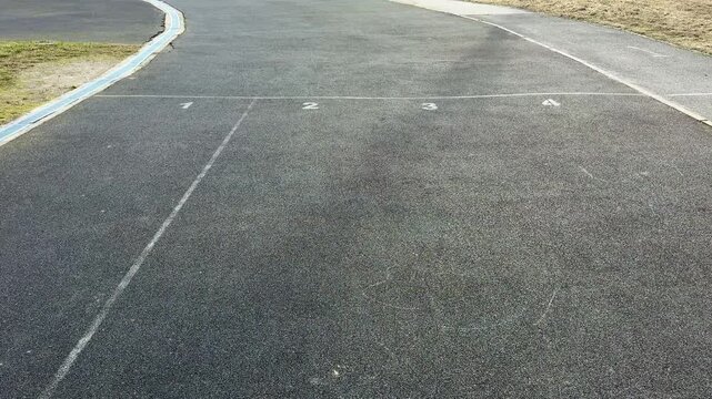 Close-up running track asphalt surface curve showing granular rubber texture, faded lane marking and grassy verge, empty prerace