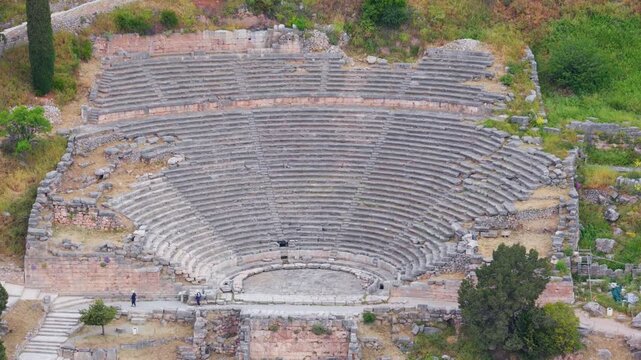 Slow zooming view of the ancient theatre of Delphi, an important archaeological site in Greece, with tourists walking through the historic ruins of the famous amphitheater built on a hillside