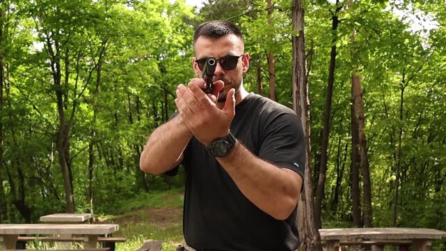 Close up of a man aiming a handgun in tactical shooting stance while raising the pistol into firing position in a forest environment, focused action training scene with defensive posture outdoors.