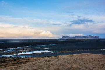Fototapeta premium Vast volcanic landscape with black sand plains and distant mountains under a cloudy sky in Iceland. High quality photo