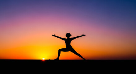 Silhouette of a woman practicing yoga warrior pose at sunset with vibrant sky