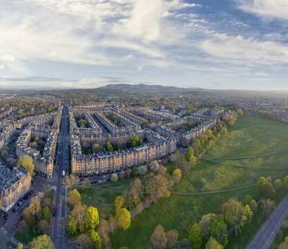 Aerial view of historic stone terraced houses bordering a lush green park under a soft blue sky with distant hills Edinburgh, Scotland, United Kingdom.