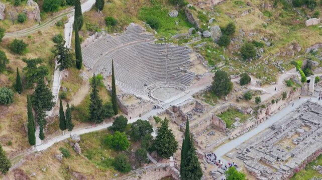 Aerial view tracking towards the ancient theatre of Delphi, an important archaeological site and popular tourist attraction showing the well-preserved stone seats and stage surrounded by mountains