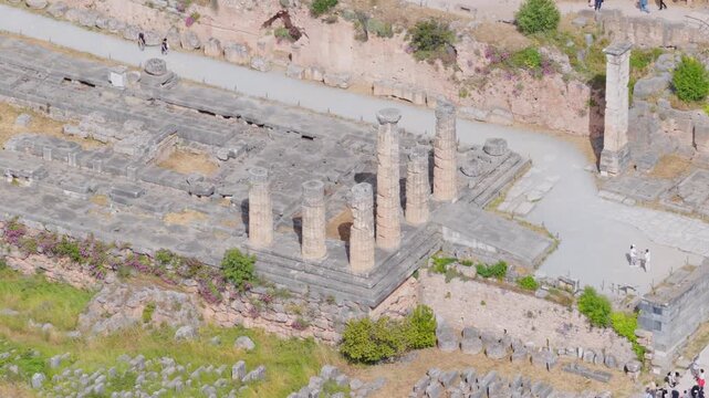 High angle view of the ancient temple of Apollo ruins at the archaeological site of Delphi, Greece, a famous Unesco world heritage site with tourists exploring the historic landmark