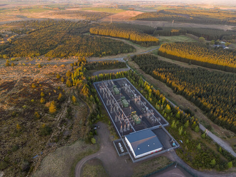 Aerial view of an electrical substation on Eaglesham moor surrounded by dense evergreen forests and open moorland during sunset Kilmarnock, Scotland, United Kingdom.