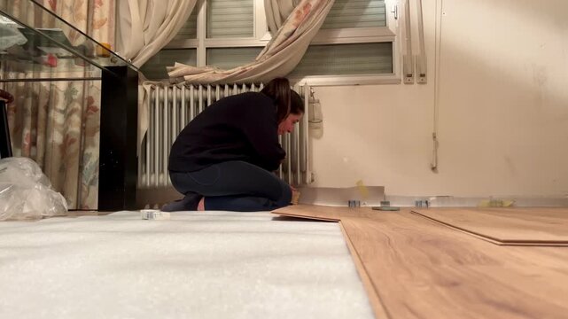 Woman installing laminate flooring using a hammer during home renovation project