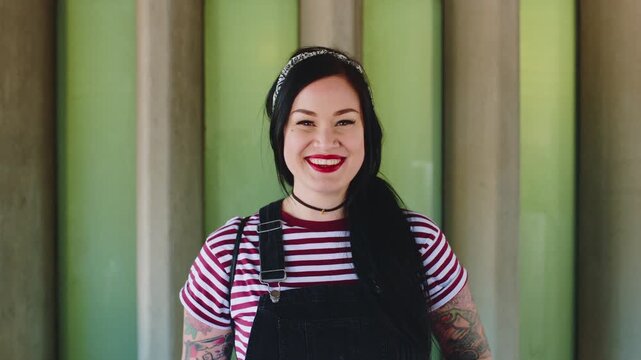 Fashion, laugh and face of woman in city for trendy clothes, style and edgy aesthetic for confidence. Happy, smile and portrait of person with cool clothing, outfit and tattoos on wall background