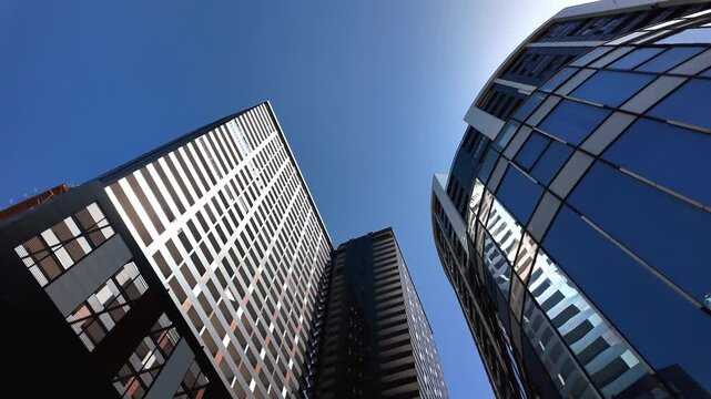 The gaze follows back past modern glass and steel skyscrapers reflecting the bright sun under clear blue skies, capturing the essence of corporate architecture and urban life