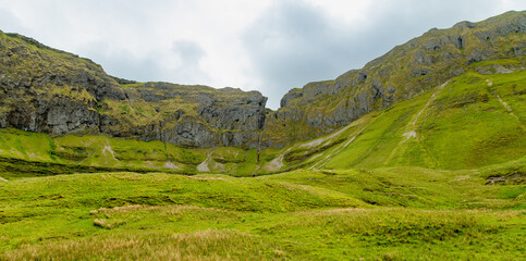 Obraz premium Gleniff Horseshoe in County Sligo, Ireland, with rolling grassland beneath steep limestone mountains and bright clouds. A scenic drive through one of Irelands classic valleys.