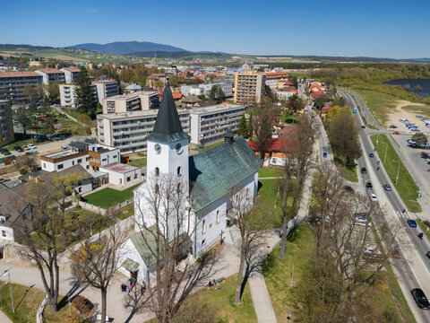 Aerial view of the Roman Catholic Church of Saints Simon and Jude with its white facade and black spire surrounded by urban buildings in Namestovo, Zilina Region, Slovakia.
