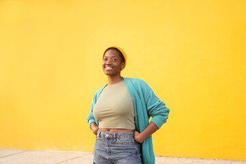 Smiling woman wearing knit cap and teal cardigan standing against bright yellow background, relaxed pose with confident expression in modern lifestyle scene © Andrii