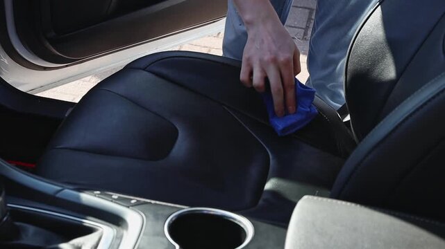 A man wipes the passenger seat of a car with a rag at a car wash.