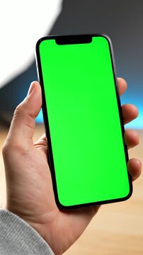 Close up of a male hand holding a futuristic slim bezel smartphone with a green screen chroma key display against a city bokeh background in natural daylight, app mockup ready