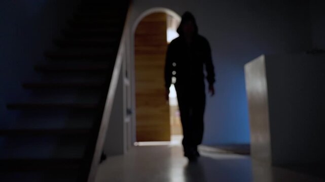 Hooded man holding a knife walking in a dark hallway