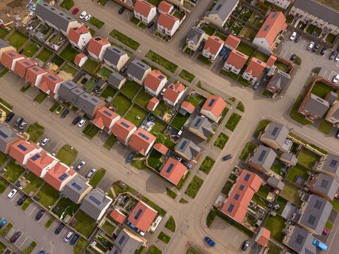 Aerial view of a modern residential neighborhood featuring rows of houses with red and grey roofs, solar panels, and private gardens in Edinburgh, Scotland, United Kingdom.