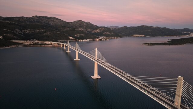 High-angle perspective of Peljesac Bridge over the Adriatic Sea during twilight. Professional drone photography of Croatia's landmark infrastructure at golden hour.