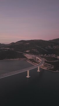 High-angle perspective of Peljesac Bridge over the Adriatic Sea during twilight. Professional drone photography of Croatia's landmark infrastructure at golden hour.