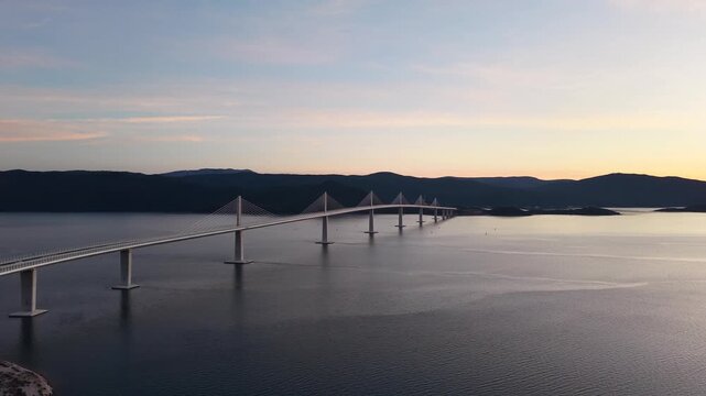 High-angle perspective of Peljesac Bridge over the Adriatic Sea during twilight. Professional drone photography of Croatia's landmark infrastructure at golden hour.
