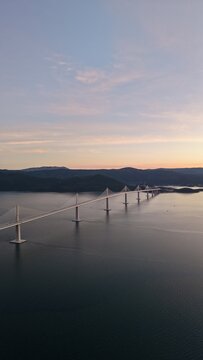 High-angle perspective of Peljesac Bridge over the Adriatic Sea during twilight. Professional drone photography of Croatia's landmark infrastructure at golden hour.