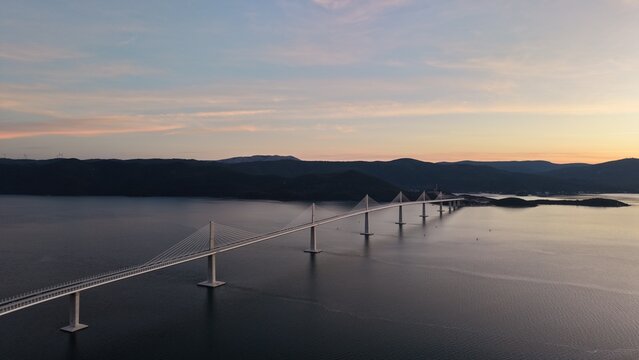 High-angle perspective of Peljesac Bridge over the Adriatic Sea during twilight. Professional drone photography of Croatia's landmark infrastructure at golden hour.