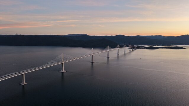 High-angle perspective of Peljesac Bridge over the Adriatic Sea during twilight. Professional drone photography of Croatia's landmark infrastructure at golden hour.