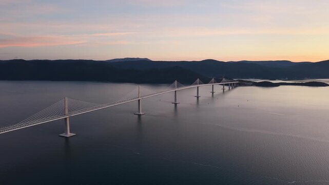High-angle perspective of Peljesac Bridge over the Adriatic Sea during twilight. Professional drone photography of Croatia's landmark infrastructure at golden hour.