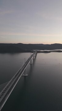 High-angle perspective of Peljesac Bridge over the Adriatic Sea during twilight. Professional drone photography of Croatia's landmark infrastructure at golden hour.