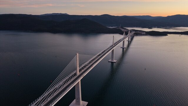 High-angle perspective of Peljesac Bridge over the Adriatic Sea during twilight. Professional drone photography of Croatia's landmark infrastructure at golden hour.
