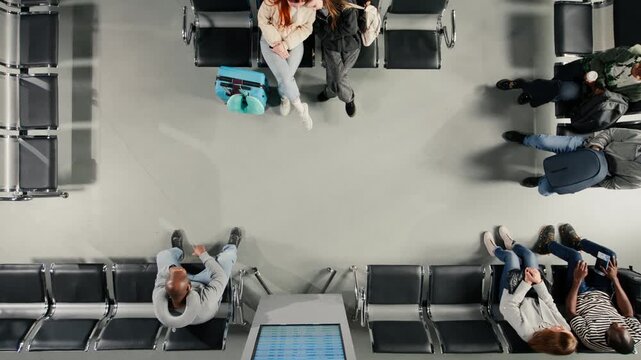 Checking departure board, timetable and airport terminal with group of passengers, top down view. Catching plane for holiday trips, FIDS screen schedule and multiethnic tourists, high angle shot