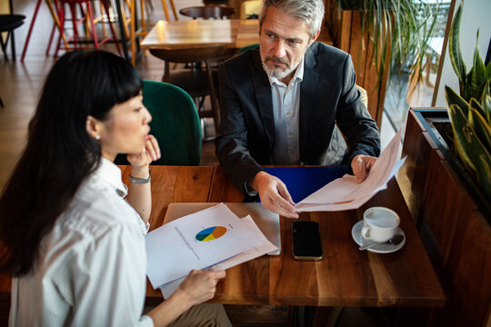 Two business professionals reviewing financial documents at a cafe table