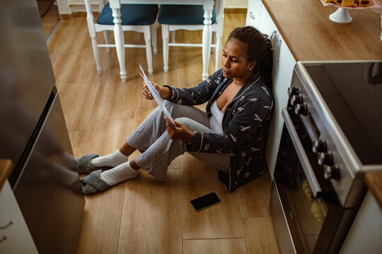 Woman reading bills on kitchen floor at home