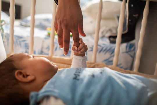 Parent holding baby's finger in a nursery crib