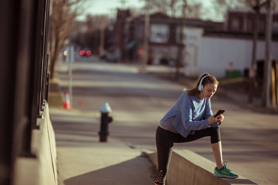 Young woman stretching with headphones before run on city sidewalk