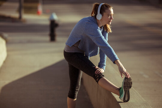 Young woman stretching before run on urban sidewalk