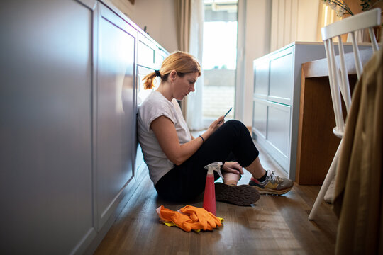 Tired woman taking a cleaning break on kitchen floor